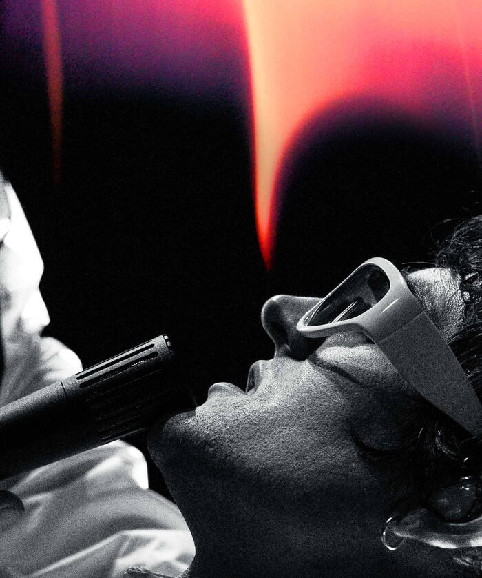 High-contrast grainy shot of a performer lit from behind by deep red stage light