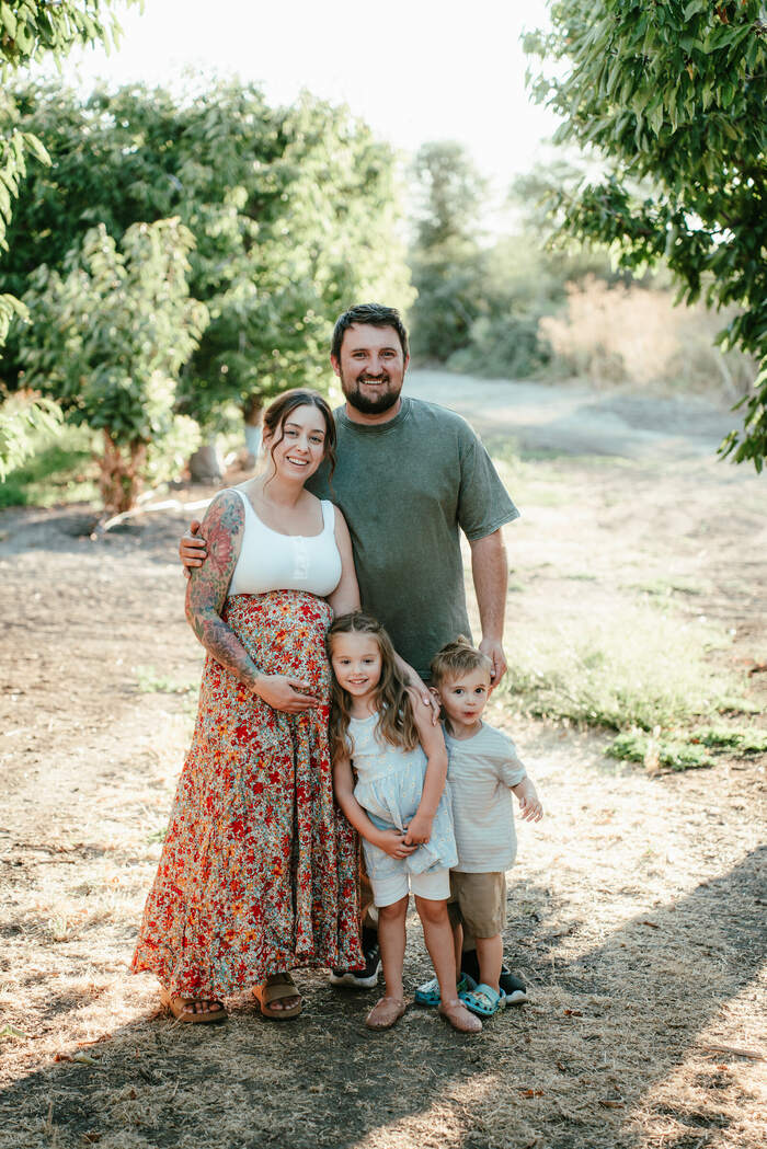 A family of four standing together on a dirt path in a sunlit orchard