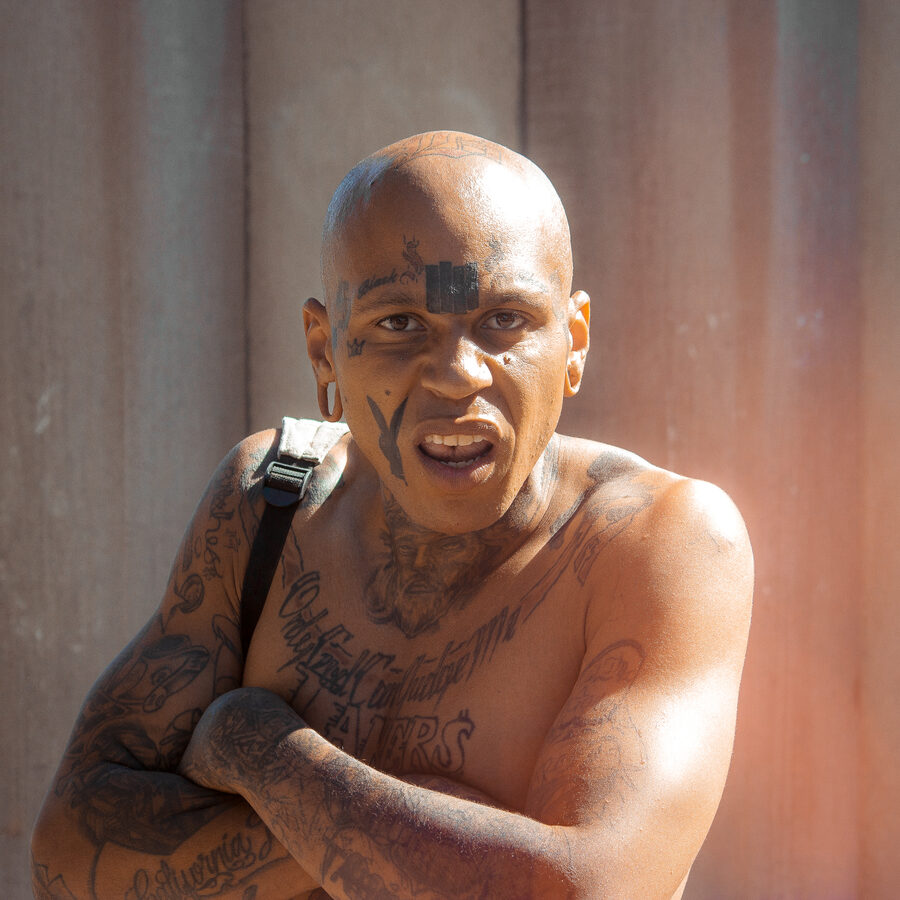 Close-up portrait of a tattooed man in warm sunlight against a muted architectural background